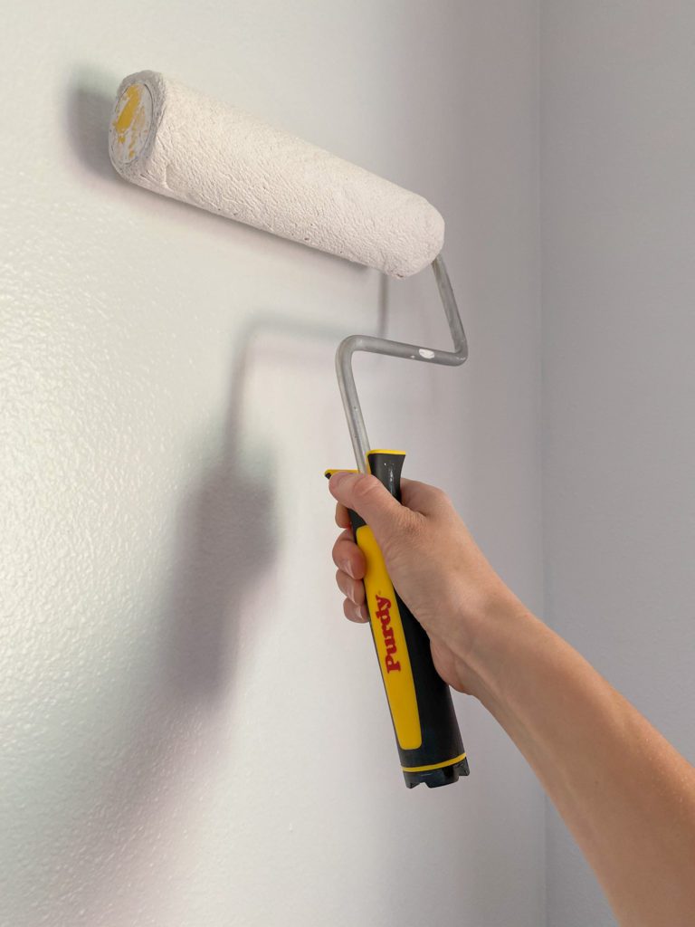 Purdy roller painting white paint on wall